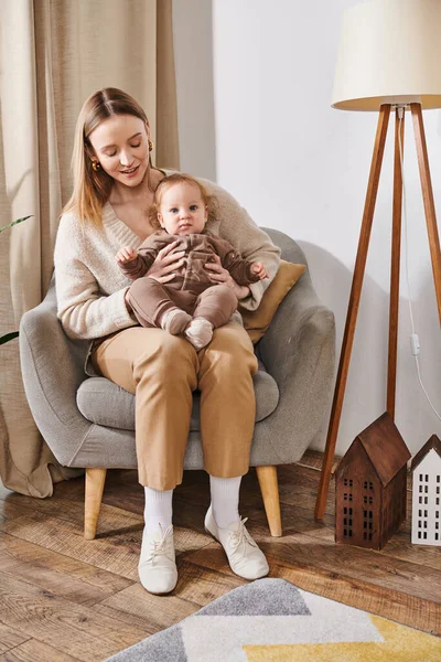 Молодая привлекательная женщина, сидящая в кресле с маленьким мальчиком в уютной детской комнате, мать и сын — стоковое фото