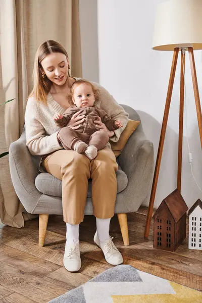 Young attractive woman sitting in armchair with baby boy in cozy nursery room, mother and son — Stock Photo