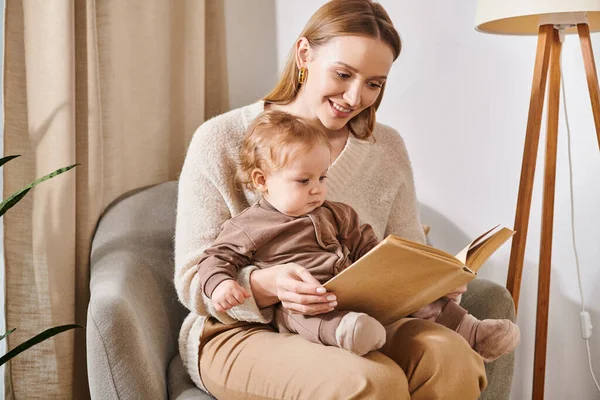 Glückliche Mutter liest Buch zu entzückenden Kleinkind Sohn im Sessel in gemütlichen Kinderzimmer, moderne Elternschaft — Stockfoto