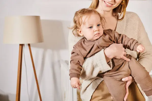 Giovane donna sorridente che tiene e abbraccia il figlio del bambino in accogliente stanza della scuola materna, beata maternità — Foto stock