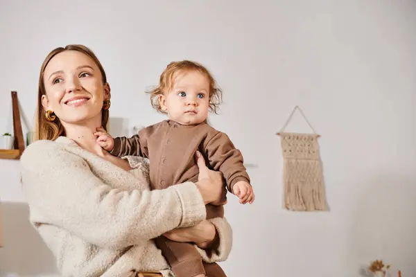Alegre sonriente mujer sosteniendo y abrazando bebé niño en acogedor cuarto de la guardería, maternidad dichosa - foto de stock