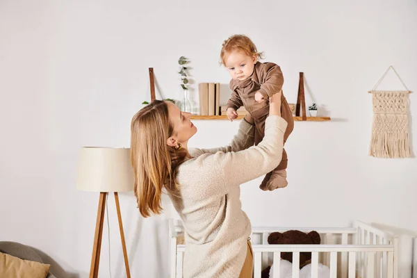 Young cheerful woman playing and having fun with cute little son in nursery room, happy motherhood — Stock Photo