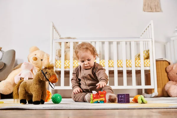 Bonito criança sentada no chão e brincando com brinquedos no quarto acolhedor berçário, infância feliz — Fotografia de Stock