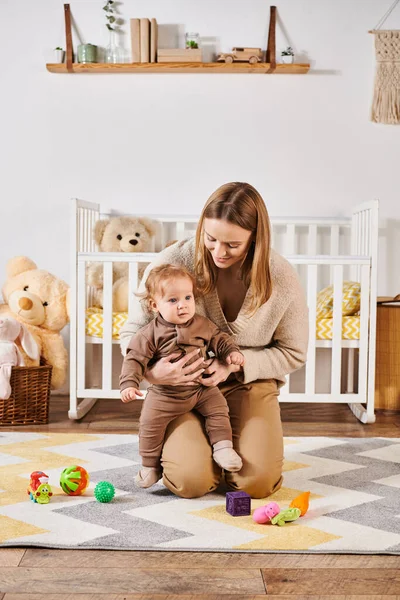 Donna gioiosa abbracciando bambino ragazzo vicino giocattoli sul pavimento in accogliente stanza dei bambini, maternità felice — Foto stock