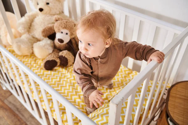 Visão de alto ângulo do menino criança em pé no berço com brinquedos macios no quarto de crianças em casa, infância — Fotografia de Stock