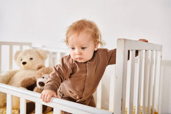 Infância feliz, menino adorável criança em pé no berço com brinquedos suaves no quarto de berçário acolhedor em casa — Fotografia de Stock