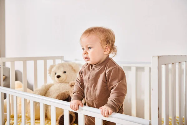 Infância feliz, menino adorável criança em pé no berço com brinquedos suaves no quarto de berçário acolhedor em casa — Fotografia de Stock