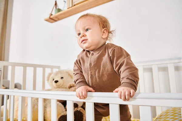 Enfance heureuse, mignon petit enfant debout dans la crèche avec des jouets mous dans une chambre d'enfant confortable à la maison — Photo de stock