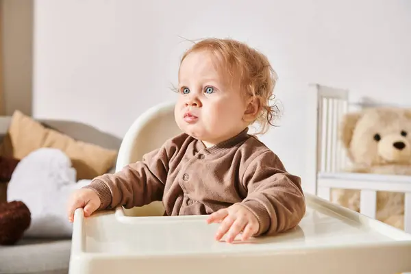 Retrato de menino criança sentada em cadeira de bebê e olhando para longe no quarto do berçário em casa — Fotografia de Stock
