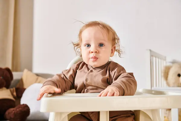 Retrato de menino bonito criança sentado em cadeira de bebê e olhando para a câmera no quarto de berçário em casa — Fotografia de Stock