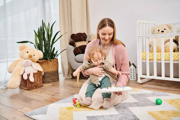 Jovem mulher alegre brincando com filho bonito criança no chão no quarto do berçário, maternidade bem-aventurada — Fotografia de Stock