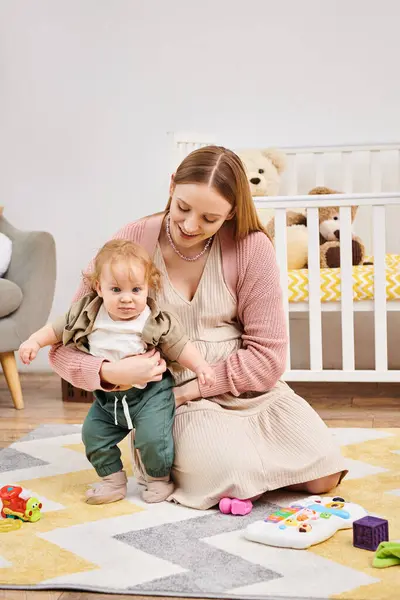 Sonriente mujer que apoya a su hijo pequeño aprendiendo a caminar en el suelo en la sala de estar en casa, maternidad - foto de stock
