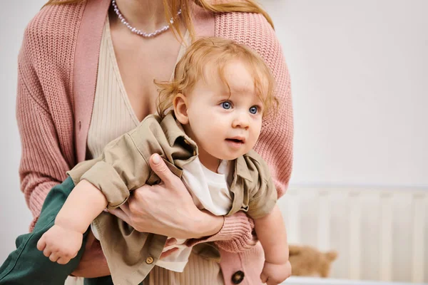 Adorable baby boy looking away in hands of his mother in nursery room at home, happy childhood — Stock Photo