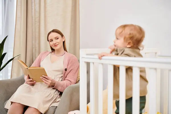 Mulher grávida feliz leitura livro perto adorável criança filho no quarto do berçário em casa, maternidade — Fotografia de Stock