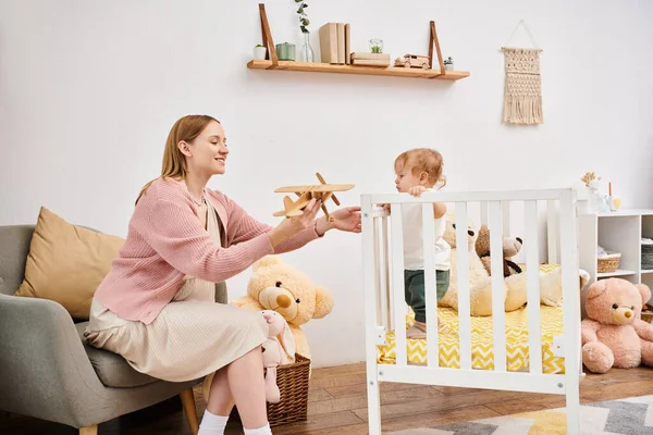 Alegre embarazada mujer celebración juguete avión cerca lindo niño hijo en cuarto de la guardería en casa, maternidad - foto de stock