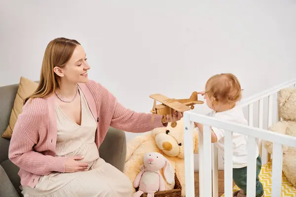Mulher grávida alegre brincando com avião de brinquedo e pequeno filho n quarto de crianças em casa, maternidade feliz — Fotografia de Stock