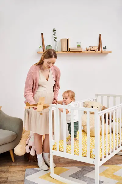 Веселая беременная женщина играет с игрушечным самолетом и малыш мальчик в детской комнате дома, материнство — стоковое фото