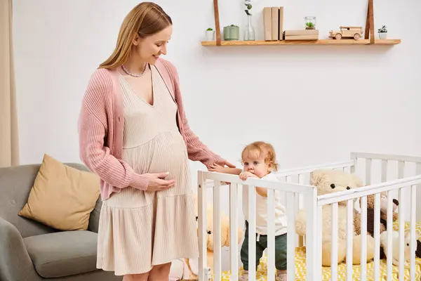 Smiling pregnant woman embracing little son standing in crib in cozy nursery room, modern parenting — Stock Photo