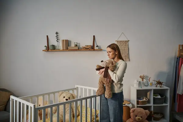 Hilflose und aufgebrachte Frau mit Stofftier steht neben Krippe in trostlosem Kinderzimmer zu Hause — Stockfoto