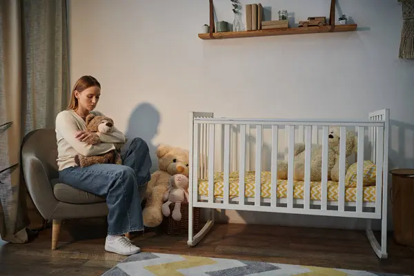 Desespero jovem mulher com brinquedo macio sentado em poltrona perto berço em quarto escuro berçário em casa — Fotografia de Stock
