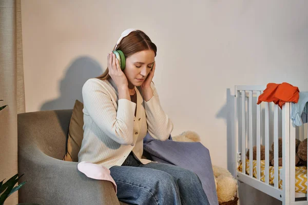 Mulher deprimida tentando relaxar ouvindo música em fones de ouvido em quarto escuro berçário em casa — Fotografia de Stock