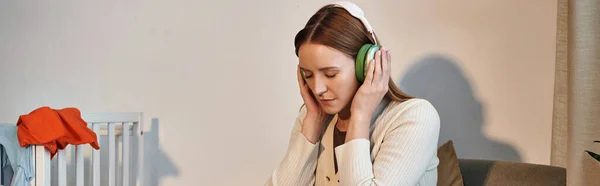 Засмучена жінка намагається розслабитися, слухаючи музику в навушниках у темній кімнаті, банер — стокове фото