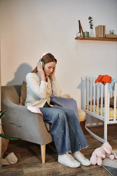 Femme frustrée essayant de se détendre en écoutant de la musique dans les écouteurs dans la chambre sombre de la pépinière à la maison — Photo de stock