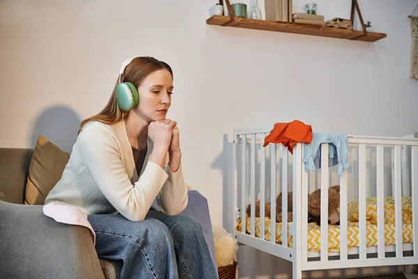 Mulher de coração pesado tentando relaxar ouvindo música em fones de ouvido em quarto escuro berçário em casa — Fotografia de Stock