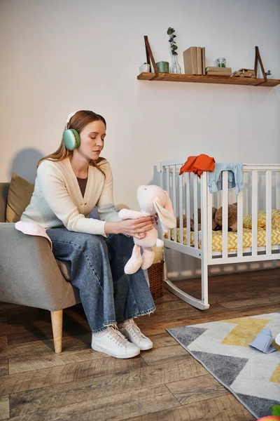 Hoffnungslose Frau mit Stofftier und Musik über Kopfhörer im dunklen Kinderzimmer zu Hause — Stockfoto