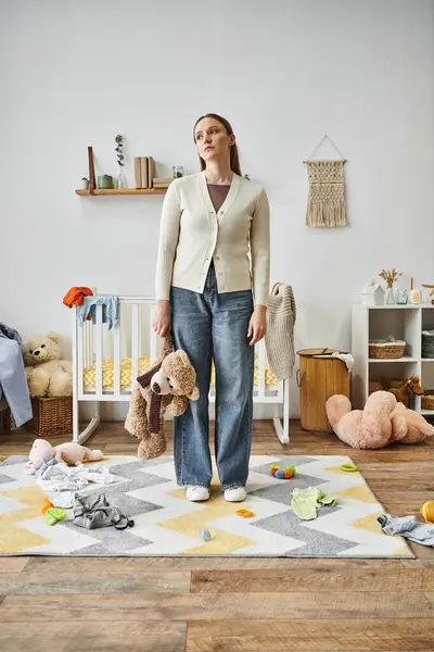 Depressed young woman with soft toy standing in nursery room at home, heartbroken moment — Stock Photo