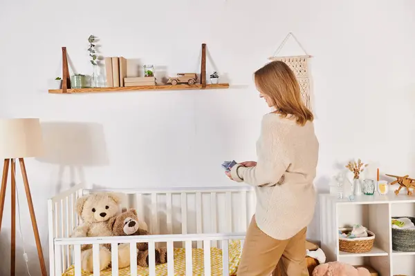 Jovem grávida de pé perto berço com brinquedos macios em quarto de crianças em casa, nova expectativa de vida — Fotografia de Stock