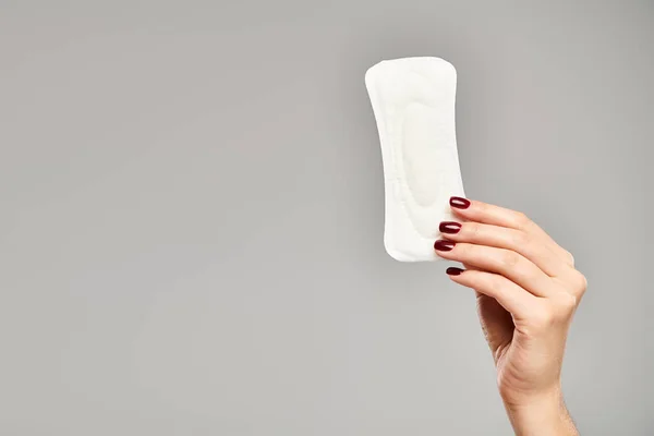 Coussin hygiénique blanc à la main de modèle féminin inconnu avec vernis à ongles sur fond gris, hygiène — Photo de stock
