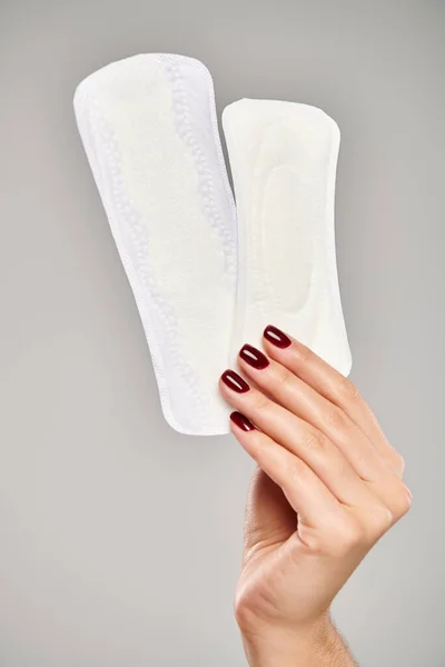 Duas almofadas menstruais brancas na mão de modelo feminino desconhecido com esmalte no fundo cinza — Fotografia de Stock