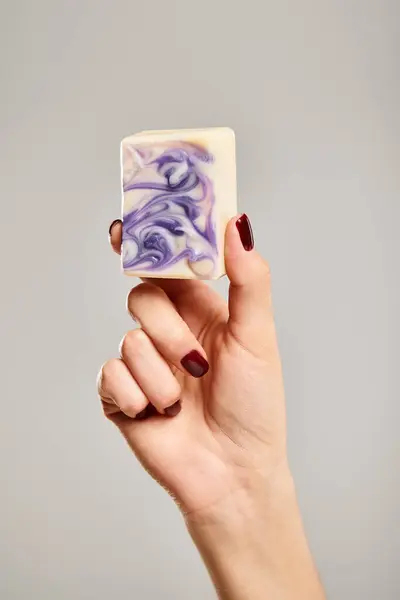 Объектное фото полосатого мыла в руке неизвестной женщины, позирующей на сером фоне — стоковое фото