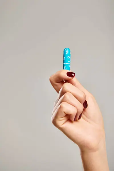 Object photo of hygienic tampon in hand of unknown woman with nail polish on gray background — Stock Photo