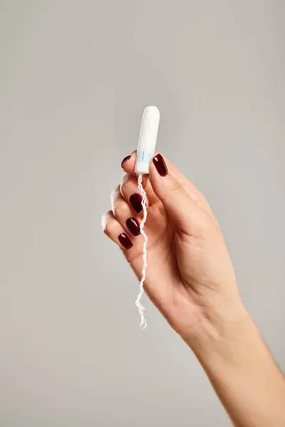 Unknown young female model with nail polish holding in hand hygienic tampon on gray background — Stock Photo