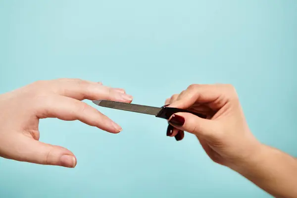 Modello femminile sconosciuto con smalto unghie limatura di un'altra donna su sfondo blu vibtant — Foto stock