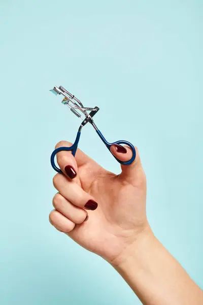 Objet photo de friseur de cils en main de jeune femme inconnue avec vernis à ongles sur fond bleu — Photo de stock