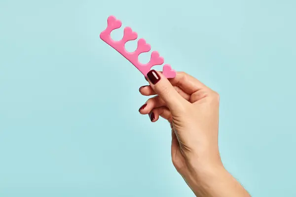 Object photo of pink toe separator in hand of unknown woman with nail polish on blue background — Stock Photo