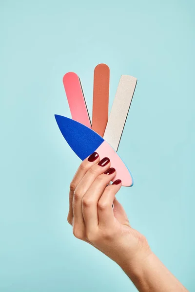 Objet photo de différentes limes à ongles en main de jeune femme inconnue avec vernis à ongles sur fond bleu — Photo de stock