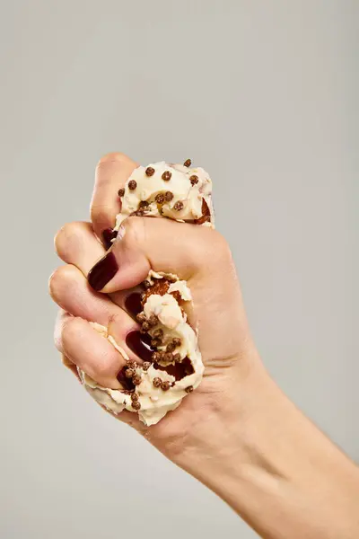 Young unknown female with nail polish squeezing delicious donut with white icing on gray backdrop — Stock Photo