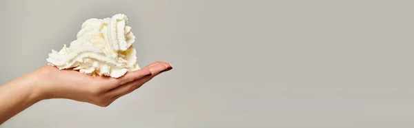 Objektfoto von köstlicher Schlagsahne in der Hand einer unbekannten jungen Frau auf grauem Hintergrund, Banner — Stockfoto