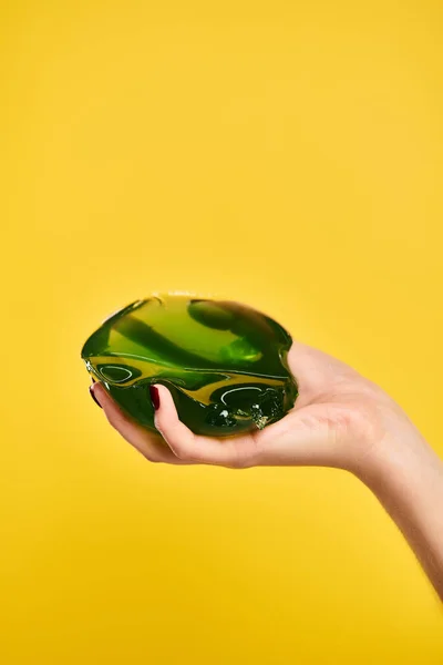 Object photo of sweet green jello in hand of young unknown female model on vibrant yellow backdrop — Stock Photo