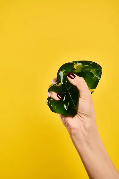 Unknown young female model squeezing mouthwatering green jello on vibrant yellow background — Stock Photo