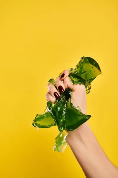 Mujer joven desconocida con esmalte de uñas apretando verde sabrosa jalea en su mano sobre fondo amarillo - foto de stock