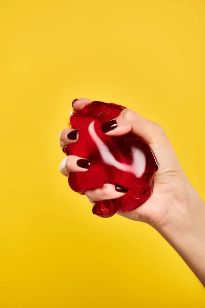 Modèle féminin inconnu avec vernis à ongles serrant gelée appétissante rouge sur fond jaune vif — Photo de stock