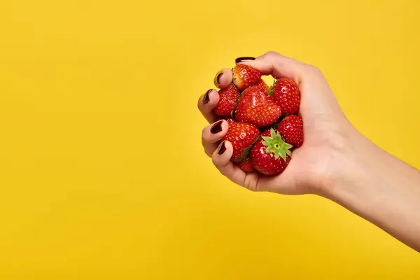Object photo of red fresh delicious strawberries in hand of young unknown woman on yellow backdrop — Stock Photo