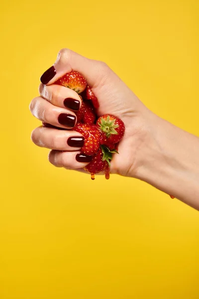 Sconosciuto giovane donna con smalto strizzando fragole fresche rosse in mano su uno sfondo vivido — Foto stock
