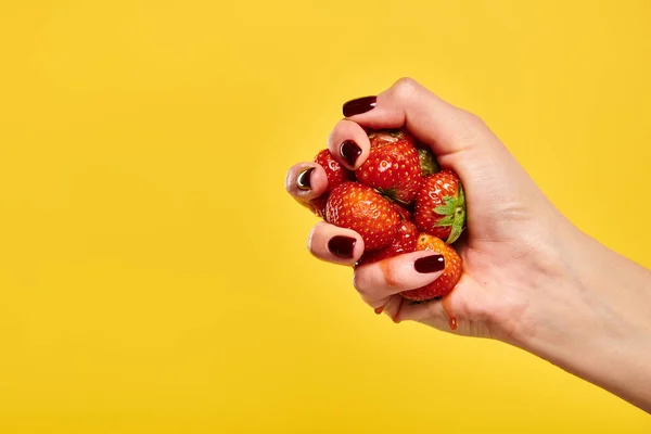 Modelo feminino desconhecido espremendo suculento deliciosos morangos em sua mão no fundo amarelo — Fotografia de Stock