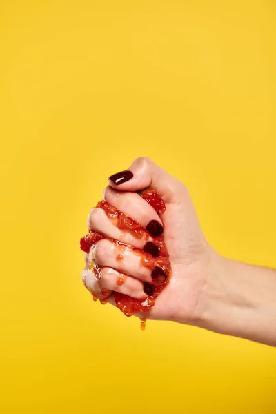 Sconosciuto giovane modello femminile spremitura rosso succosa fragole in mano su sfondo giallo — Foto stock